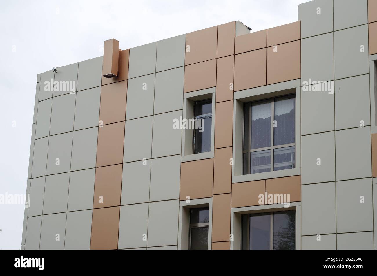 The beige and brown facade of a modern building against an overcast sky. Daytime. Shooting in the rain. Architecture. Stock Photo