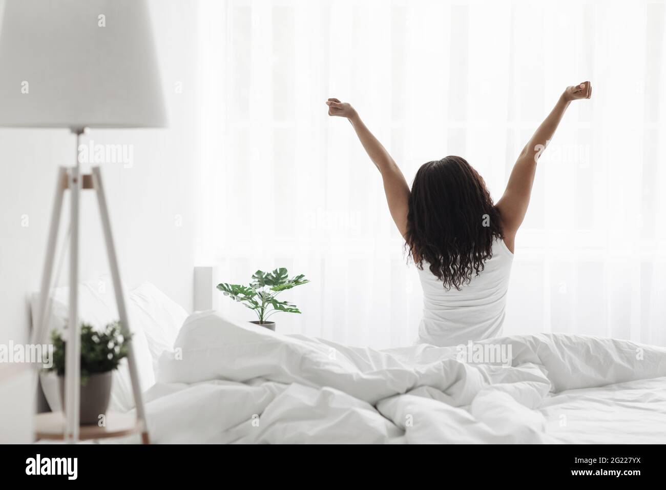 Good morning. Well-rested african american lady stretching on bed, enjoying new day, back view, free space Stock Photo