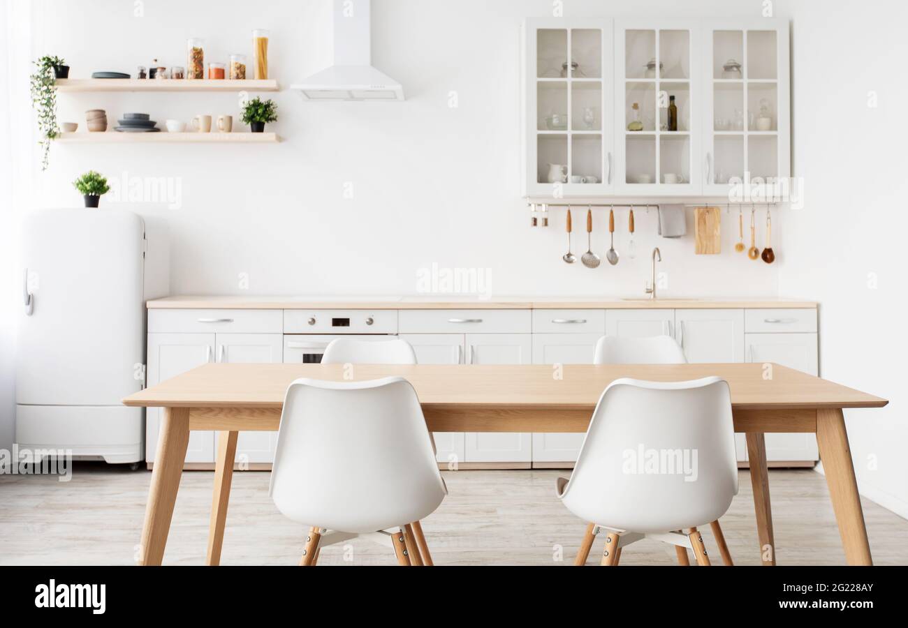 Scandinavian interior design. Light kitchen furniture and dining table, different utensils and kitchenware on shelves Stock Photo