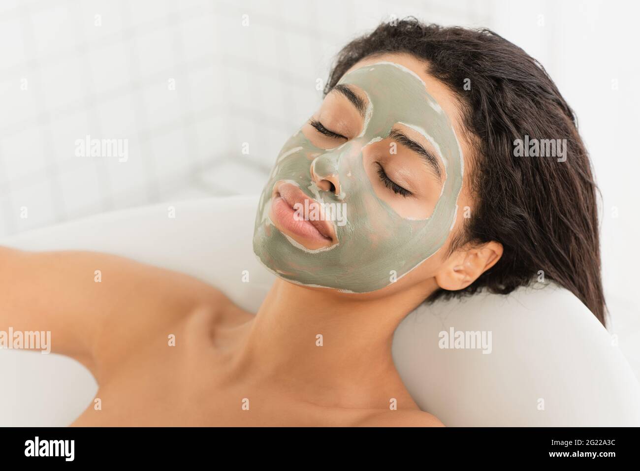 relaxed young african american woman with mud mask on face lying in