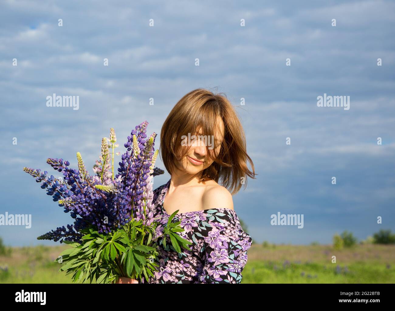 Happy woman's face covered with hair against blue sky. In the hands of a bouquet of wild flowers. atmospheric photo, flowering season, carefree day. d Stock Photo