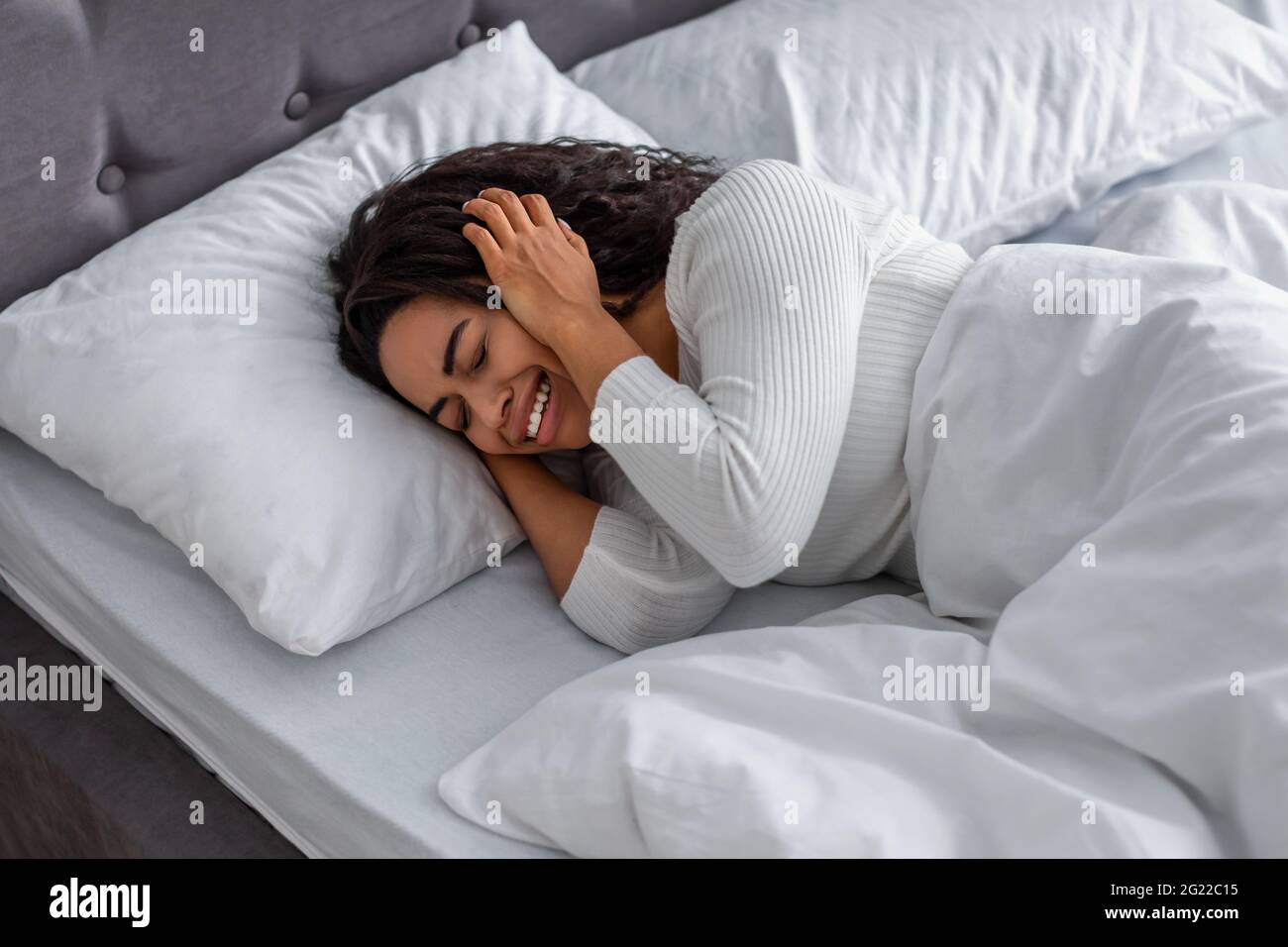 Black woman crying, lying in bed covering face Stock Photo