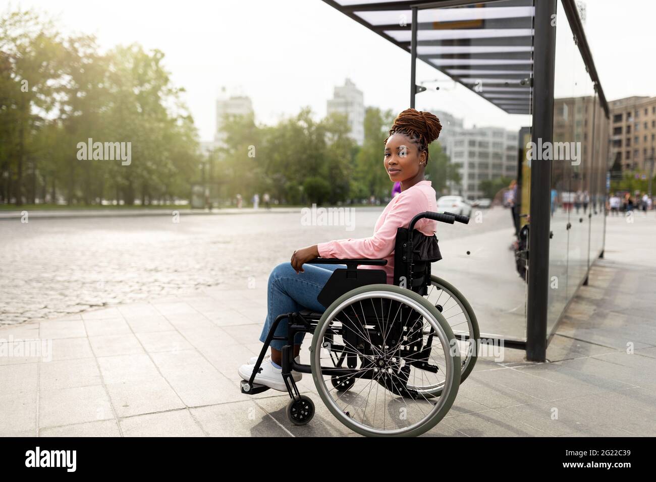 Young black handicapped woman in wheelchair cannot board vehicle suitable for impaired persons, waiting on bus stop Stock Photo