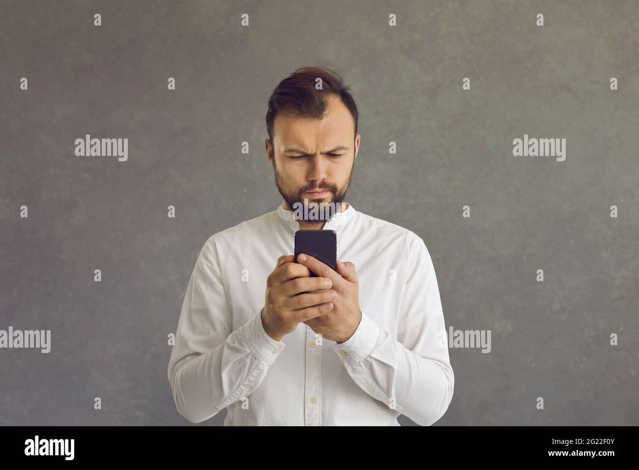 Serious businessman using smartphone standing over grey studio background Stock Photo