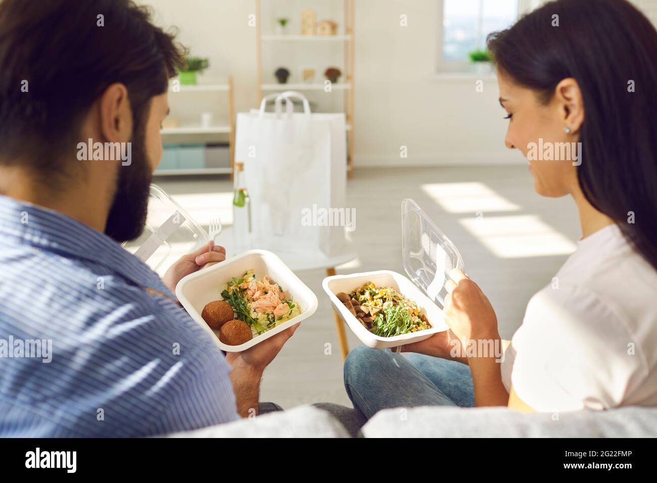 Happy young man and woman sitting on couch at home and enjoying healthy takeaway lunch Stock Photo