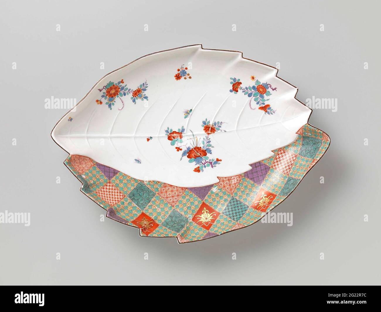 Dish, painted multi-colored with a hop of cake and an Imii decor. Dish of painted porcelain. The dish has the shape of two partially covering leaves. The edge is partly serrated. One leaf has a large grain with being ververrings and is painted with flower branches. The other half-covered leaf is painted with a pressure Imari textile pattern of windows. The dish has been marked. Stock Photo