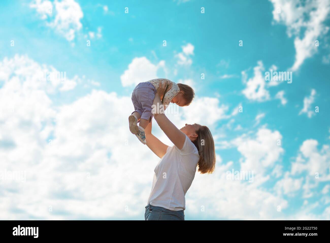 Young happy mother throws up baby in the sky. Side view. Bottom view ...