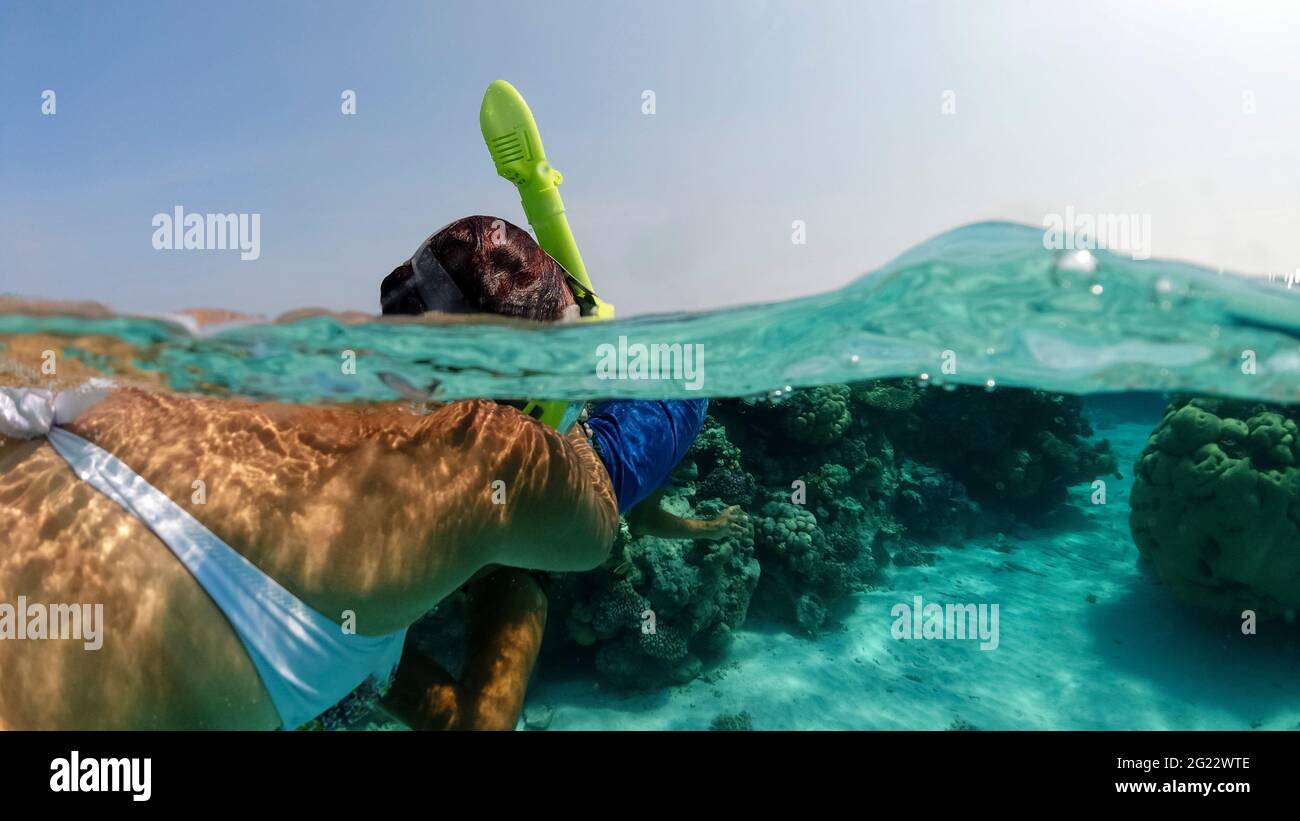 Summer vacation snorkeling in the ocean near the diving reef. A masked tourist looks at the sandy bottom under water. Underwater split photos Stock Photo