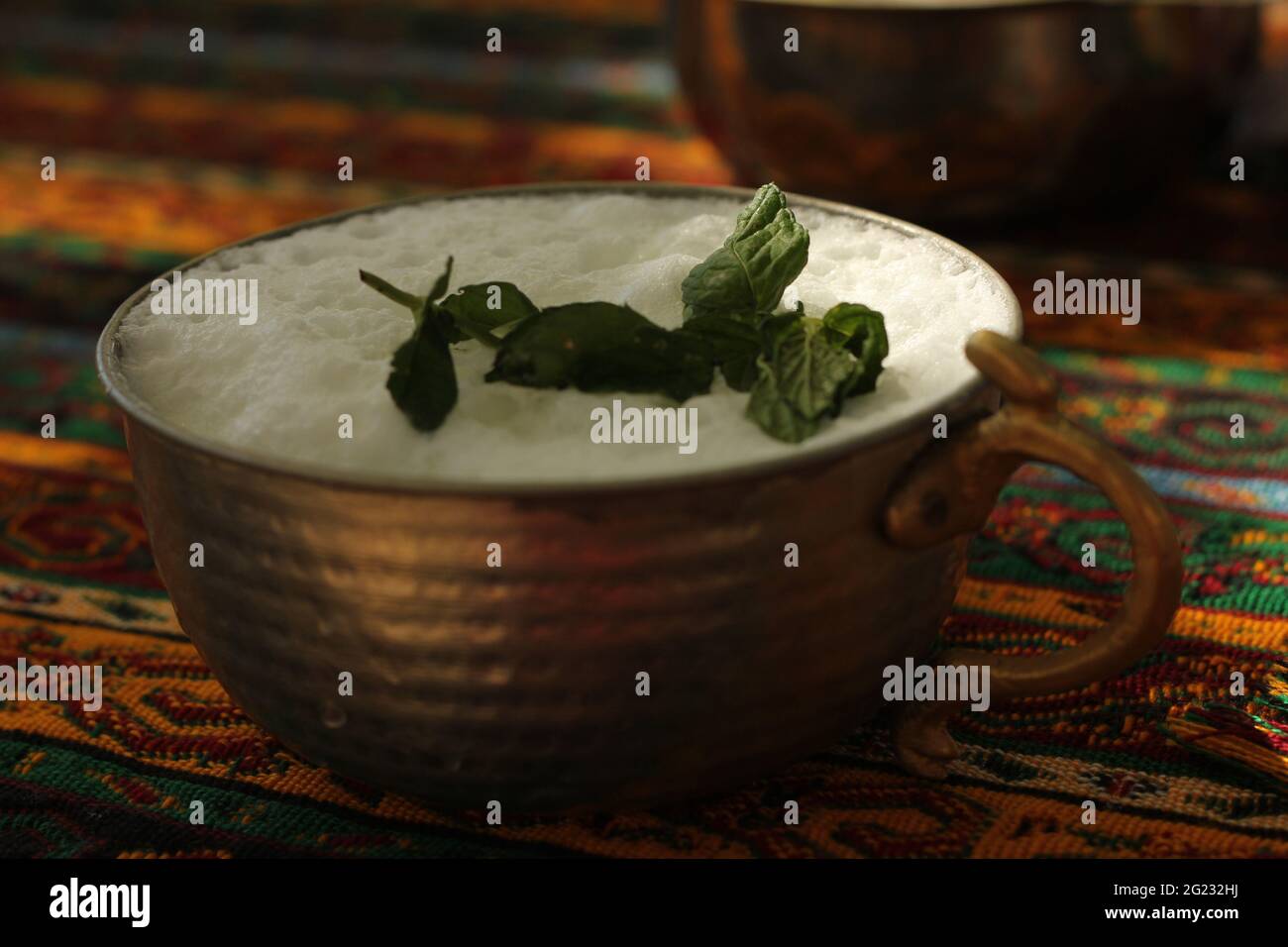 Natural healthy beverage drink ayran served in traditional handmade Anatolian copper cup decorated with fresh mint leaves. Stock Photo