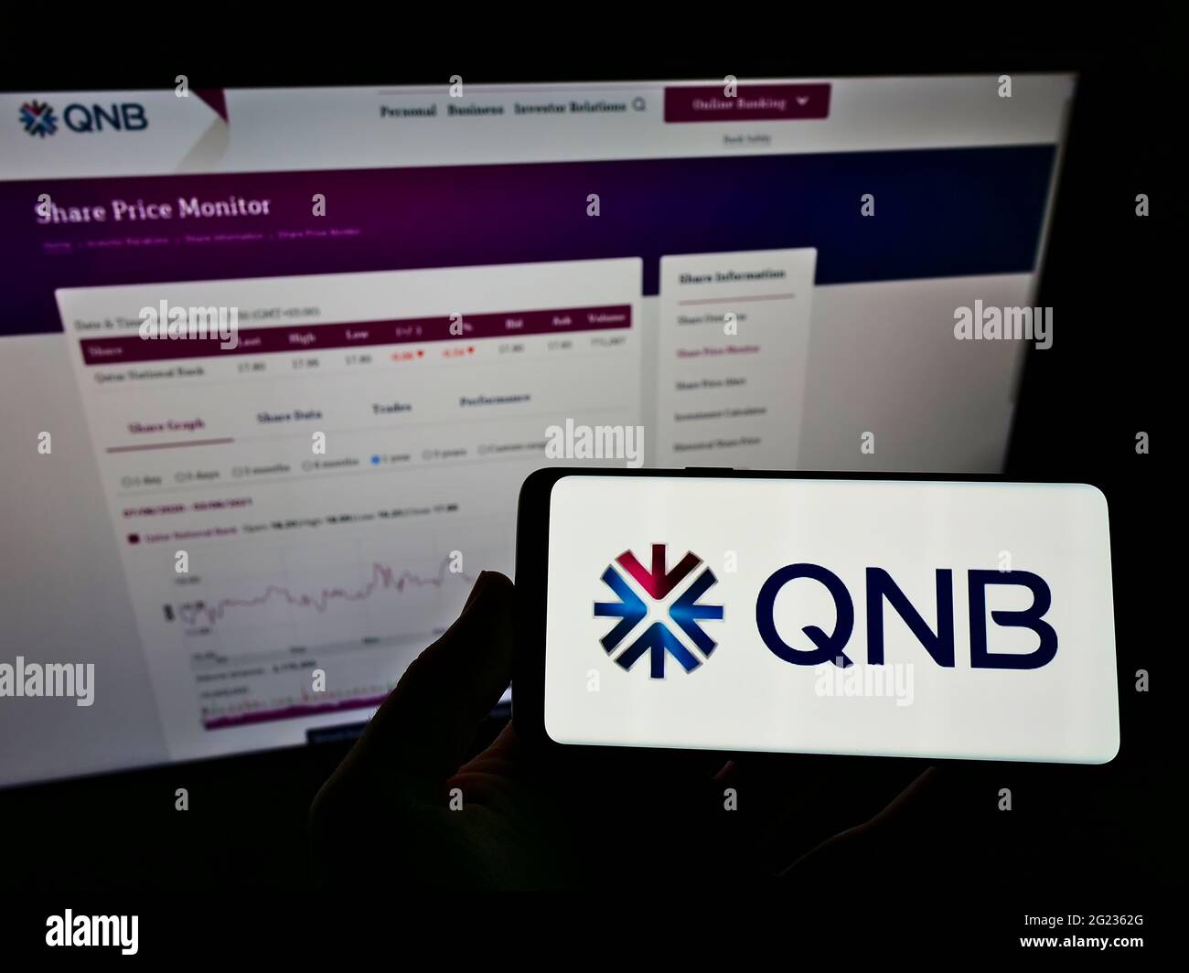 Person holding smartphone with logo of financial company Qatar National Bank Q.P.S.C. (QNB) on screen in front of website. Focus on phone display. Stock Photo