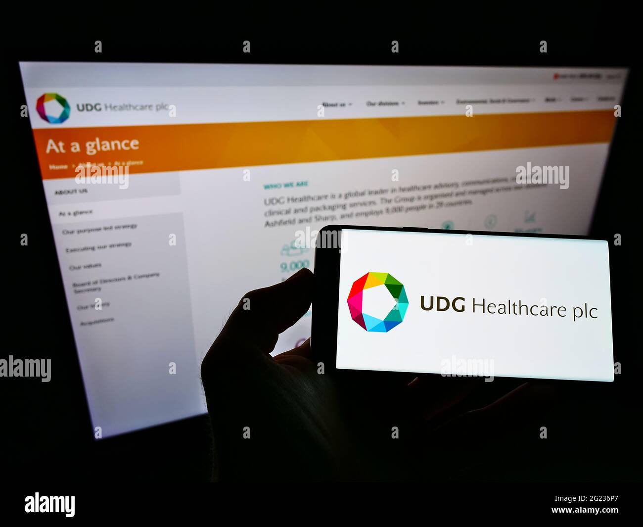 Person holding cellphone with logo of Irish pharmaceutical company UDG Healthcare plc on screen in front of business webpage. Focus on phone display. Stock Photo