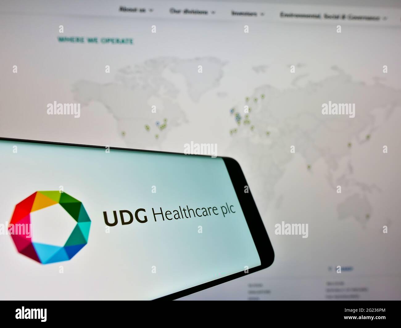 Cellphone with logo of Irish pharmaceutical company UDG Healthcare plc on screen in front of website. Focus on center-right of phone display. Stock Photo