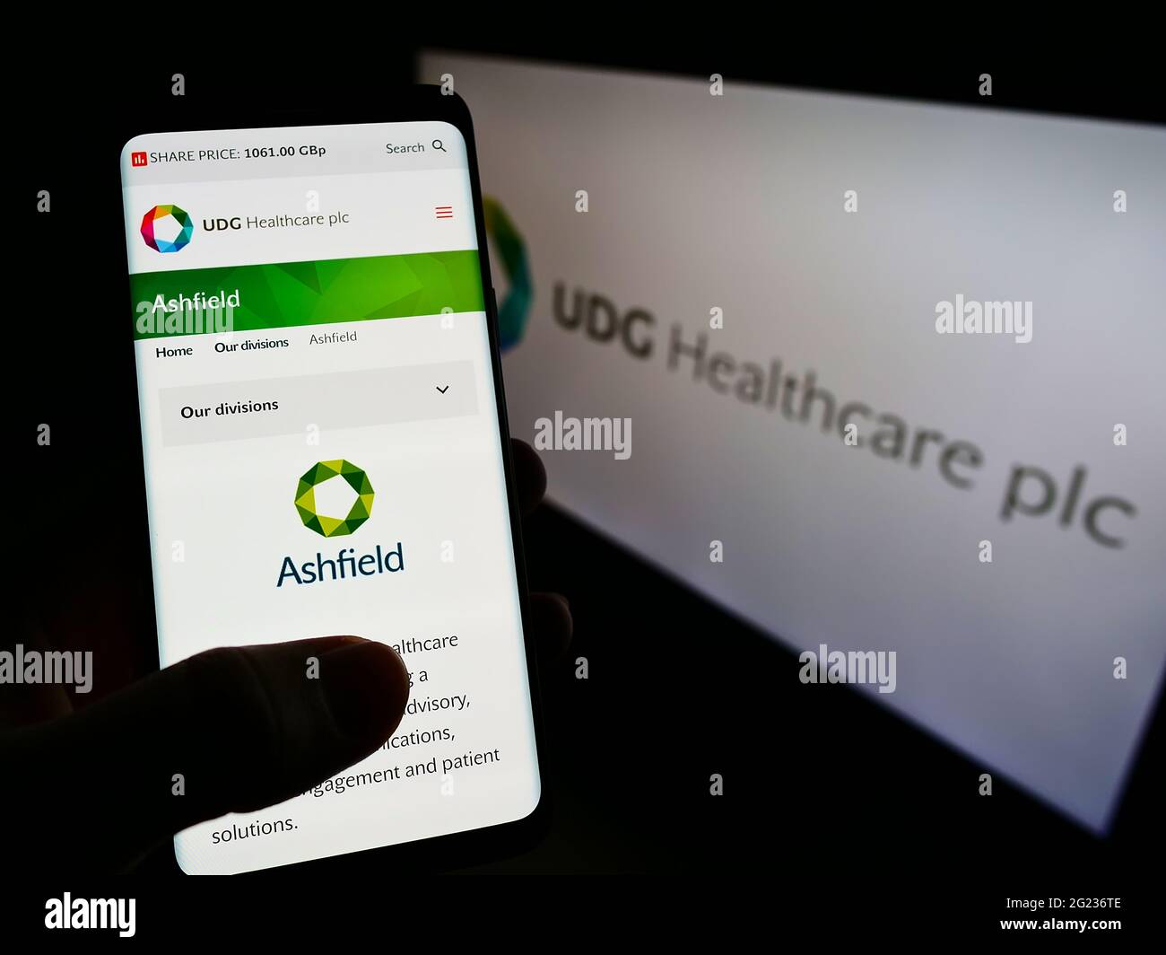 Person holding smartphone with website of Irish pharmaceutical company UDG Healthcare plc on screen with logo. Focus on center of phone display. Stock Photo
