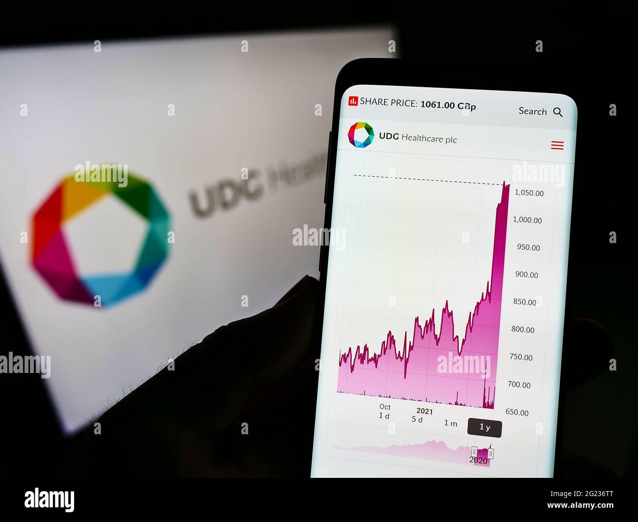 Person holding cellphone with webpage of Irish pharmaceutical company UDG Healthcare plc on screen with logo. Focus on center of phone display. Stock Photo