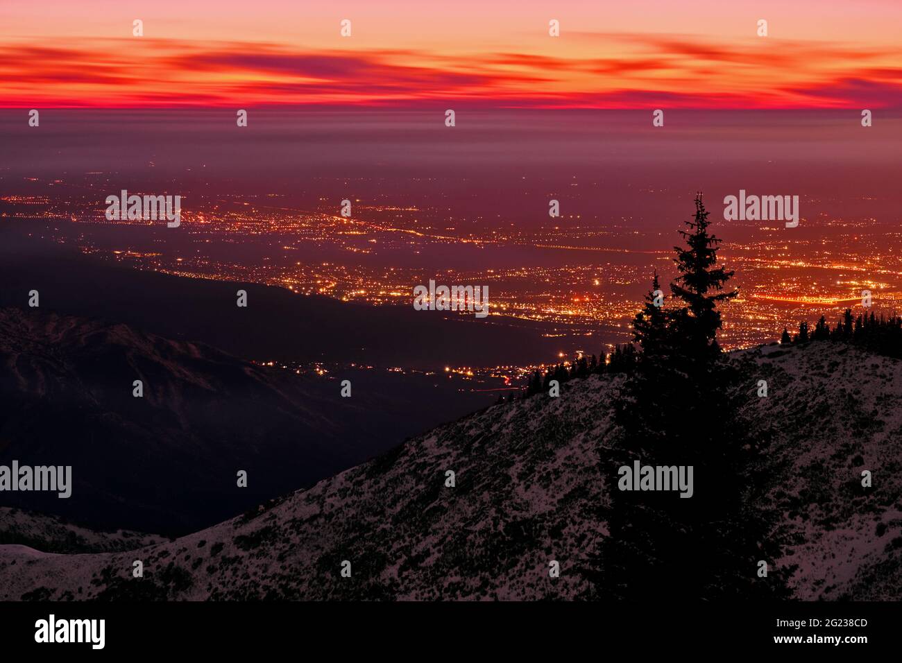 Aerial view of snow-capped mountains on the background of night city lights and sunset clouds Stock Photo