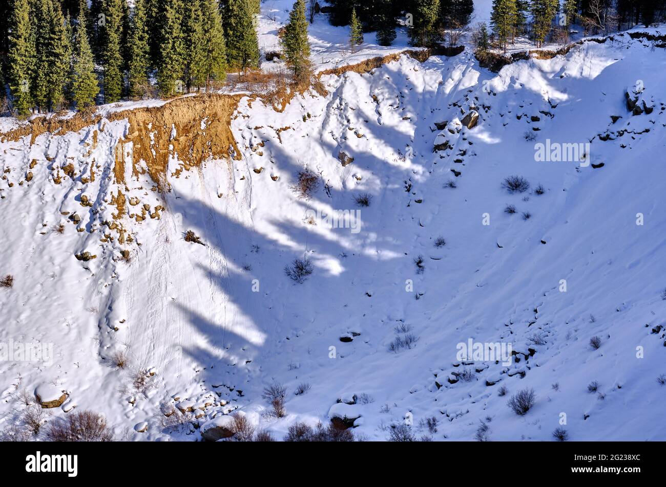 Interestingly shaped shadows cast by a number of fir trees on the snow in a mountain valley in the winter season Stock Photo