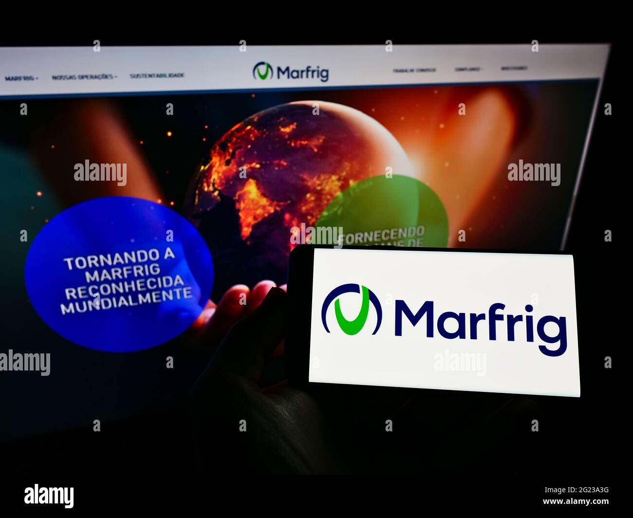 Person holding cellphone with logo of Brazilian food company Marfrig Global Foods SA on screen in front of business webpage. Focus on phone display. Stock Photo