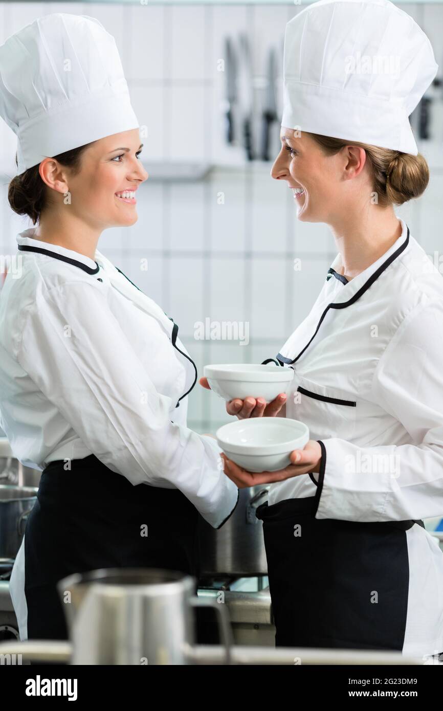 Two female chefs in gastronomic kitchen wearing white cooking uniforms