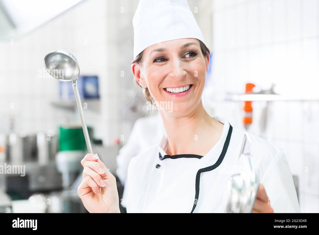Smiling chef in commercial kitchen waving ladle Stock Photo Alamy