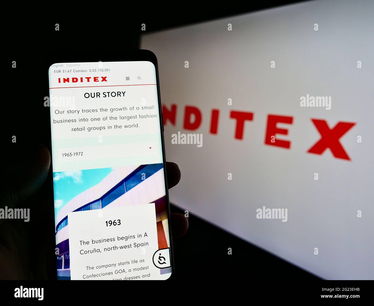 Person holding mobile phone with webpage of Spanish Industria de Diseño Textil S.A. (Inditex) on screen with logo. Focus on center of phone display. Stock Photo