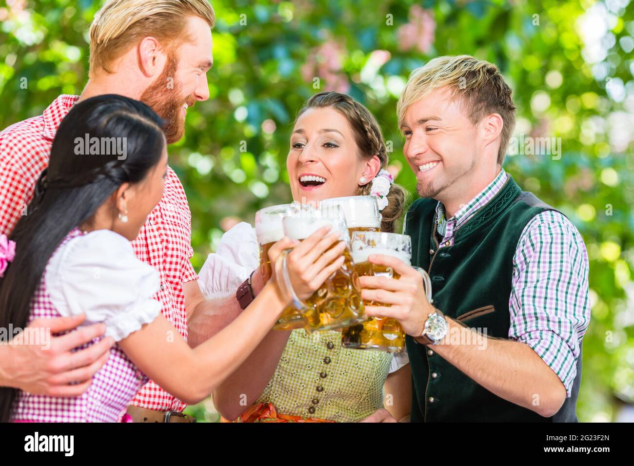 Friends, two men, two women, standing in beer garden clinking glasses with beer Stock Photo