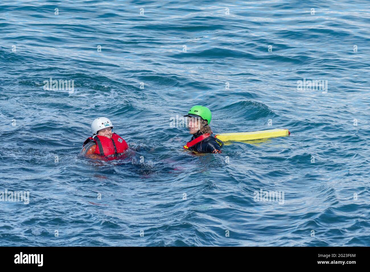 A coasteering guide floating in the sea with a holidaymaker on the coast of Towan Head in Newquay in Cornwall. Stock Photo