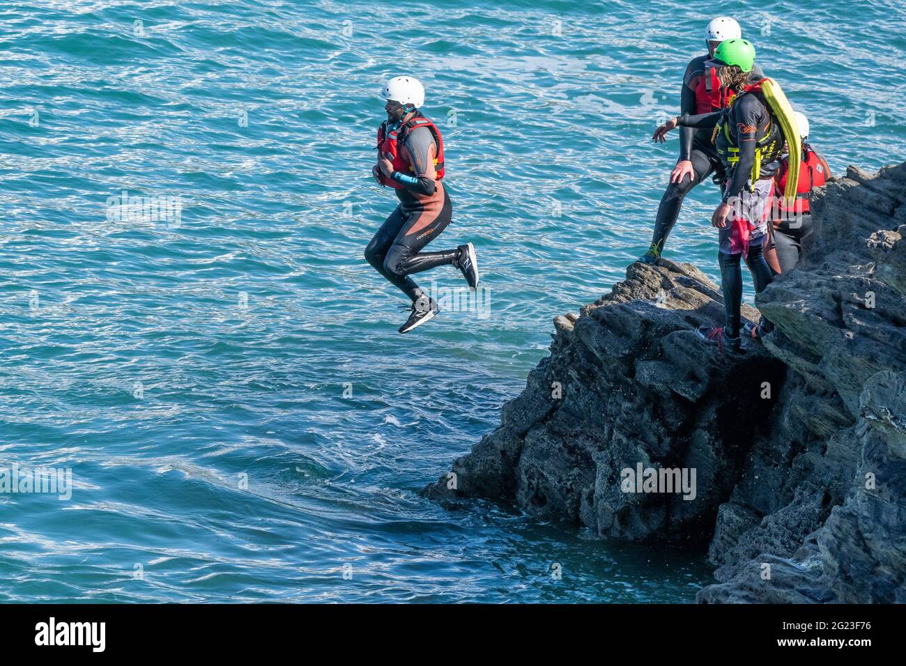 Holidaymakers jumping off rocks coasteering with a guide on Towan Head in Newquay in Cornwall. Stock Photo