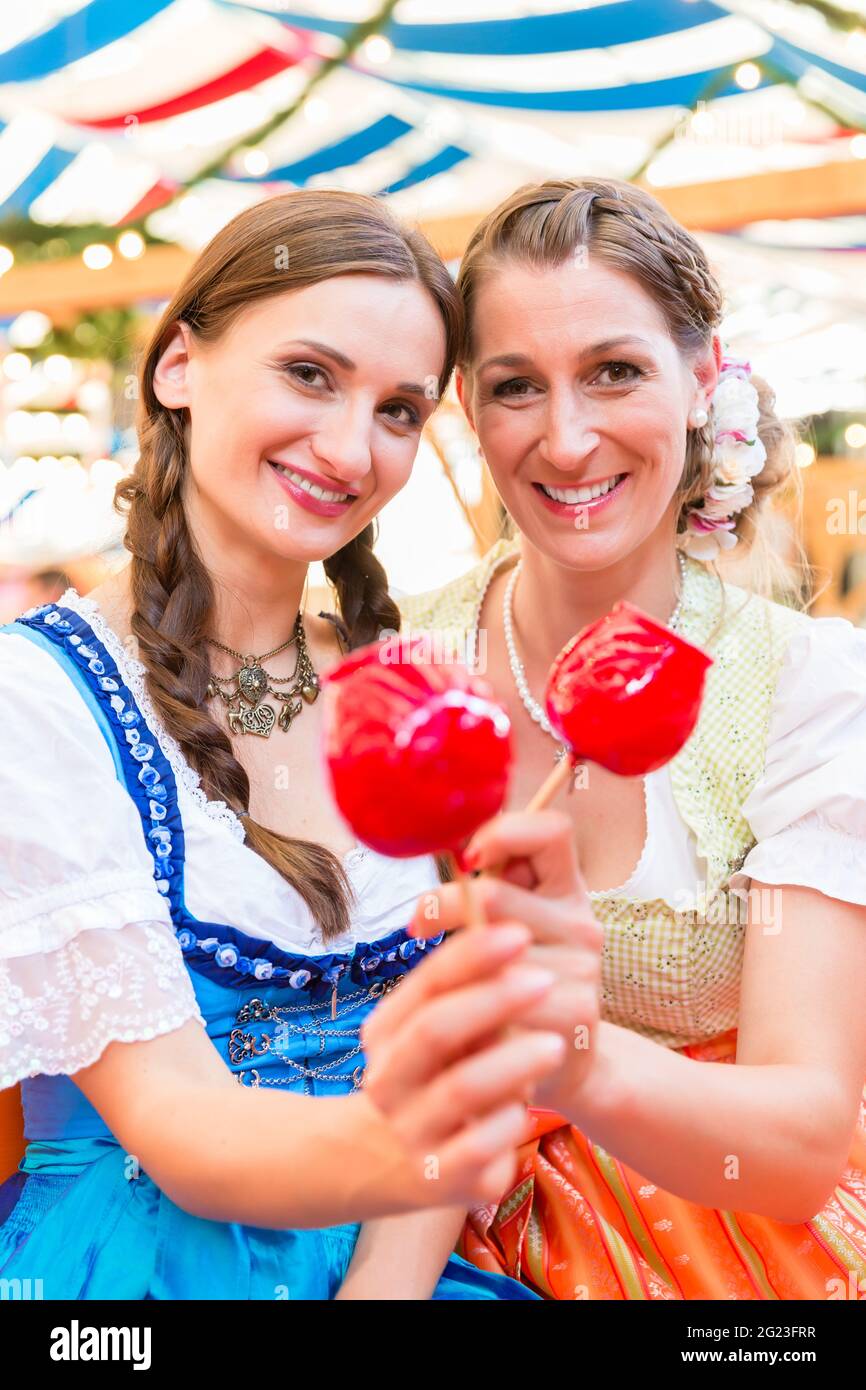 two-friends-wearing-dirndl-and-holding-candy-apples-in-a-beer-tent-at