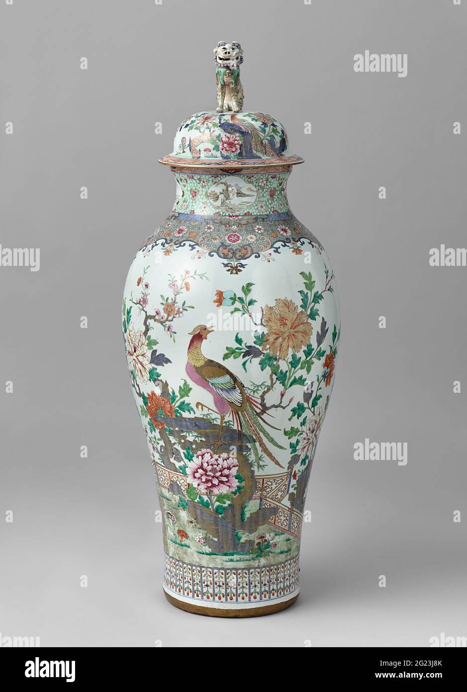 Baluster Covered Jar With Pheasants on a Rock Near a Fence and Flowering Plants. Porcelain baluster-shaped lid, painted in underglaze blue and on the glaze in blue, red, pink, green, yellow, black and gold. On the wall a pheasant on a rock in blooming plants (peony, prunus) and a fence. A second pheasant, butterflies and birds flies in the air. On the ground other flowers (Aster, Lotus, Prachtanjer), mushrooms (Lingzhi) and a pond with ducks. On the edge in Imii colors with a band with clouds on arrears interrupted by cartouches with lotus drinks. Cover knob in the shape of a shishi. Family Ro Stock Photo