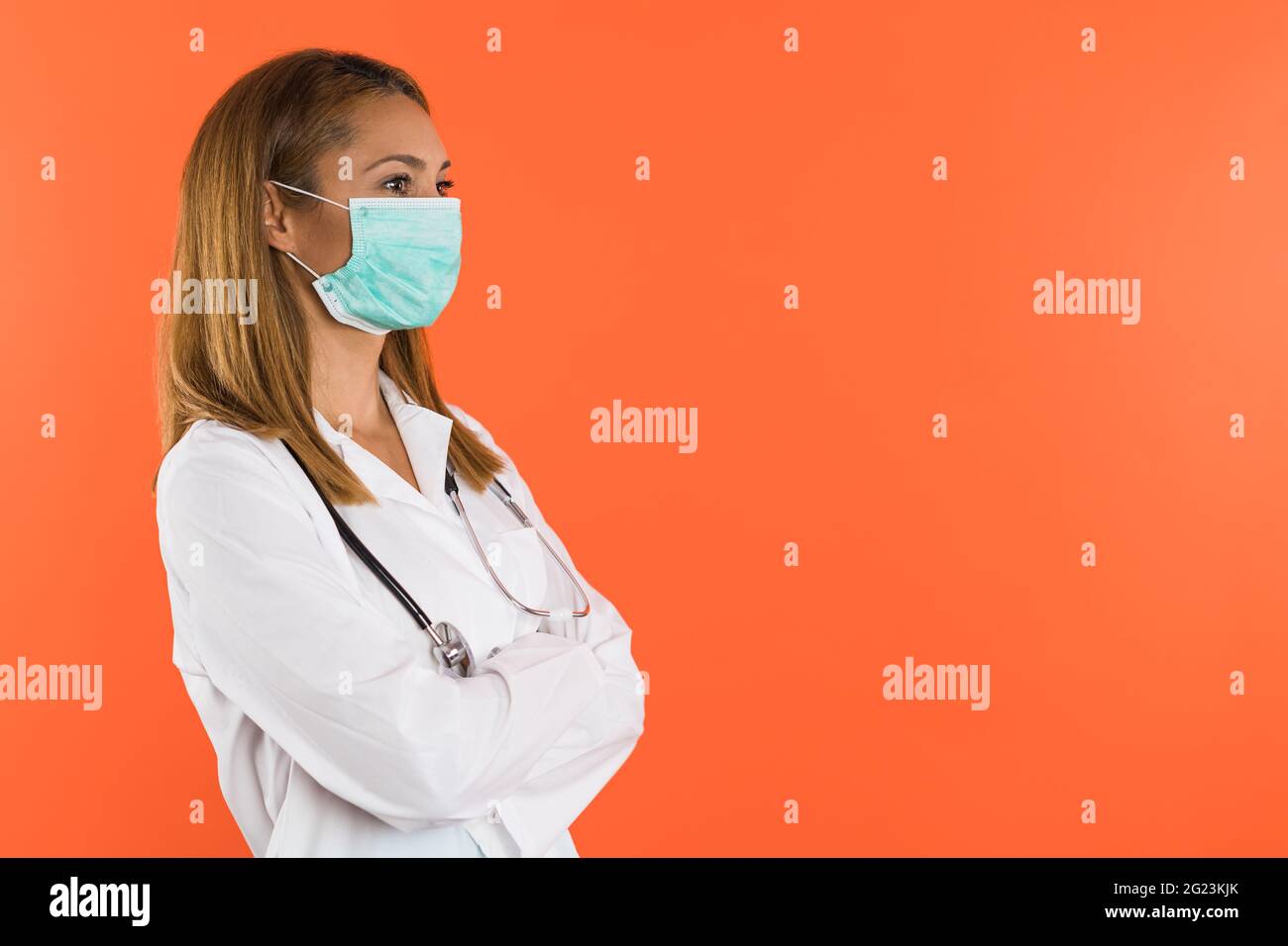 Female doctor or nurse with face mask poses in profile, wearing white coat Stock Photo