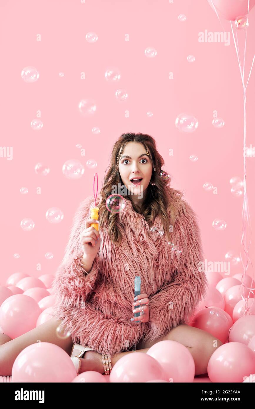 Young pretty woman having fun with soap bubbles on pink background with balloons. Party, celebration, fun concept Stock Photo