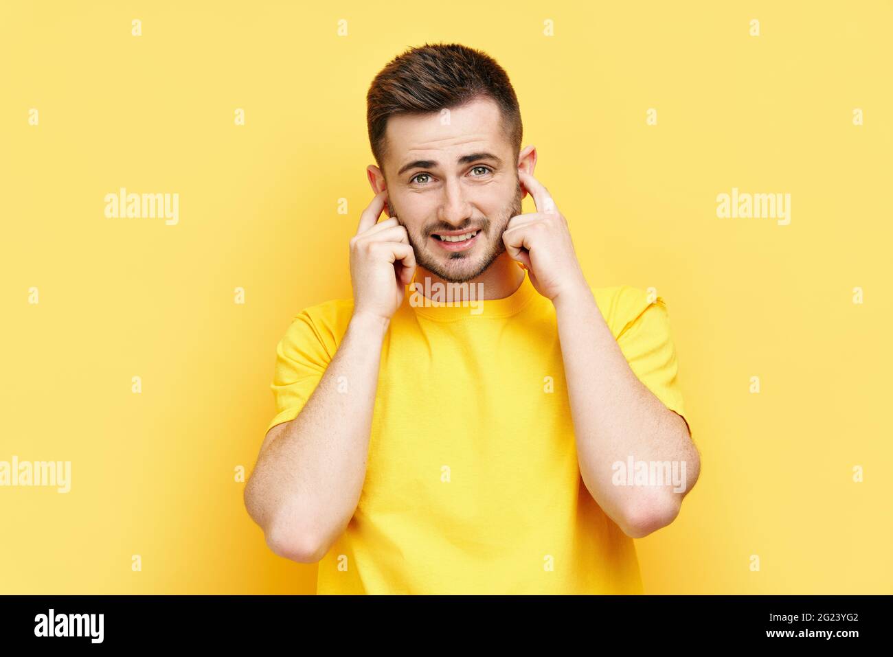 Handsome funny man covering his ears with hands afraid to hear bad news isolated on yellow background. silence concept Stock Photo