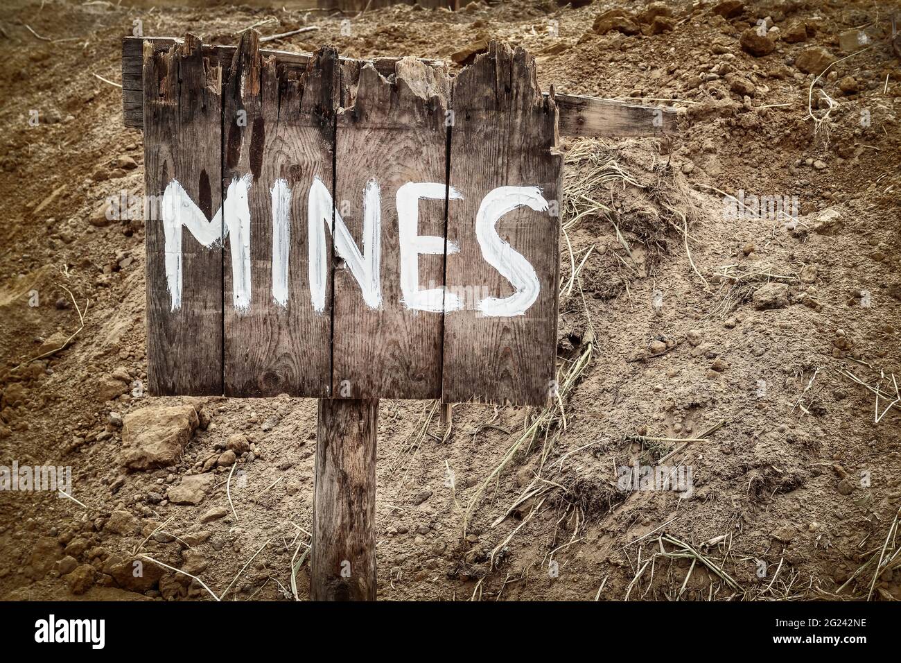 Wooden weathered warning sign for mines in front of a minefield Stock Photo