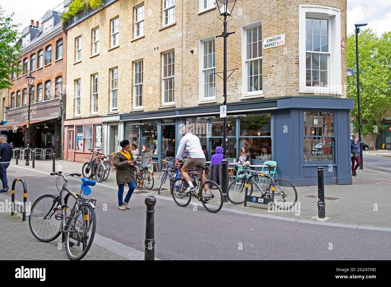 People cycling walking outside Briki restaurant & Exmouth Market street sign on building in Clerkenwell Islington London EC1 England UK  KATHY DEWITT Stock Photo
