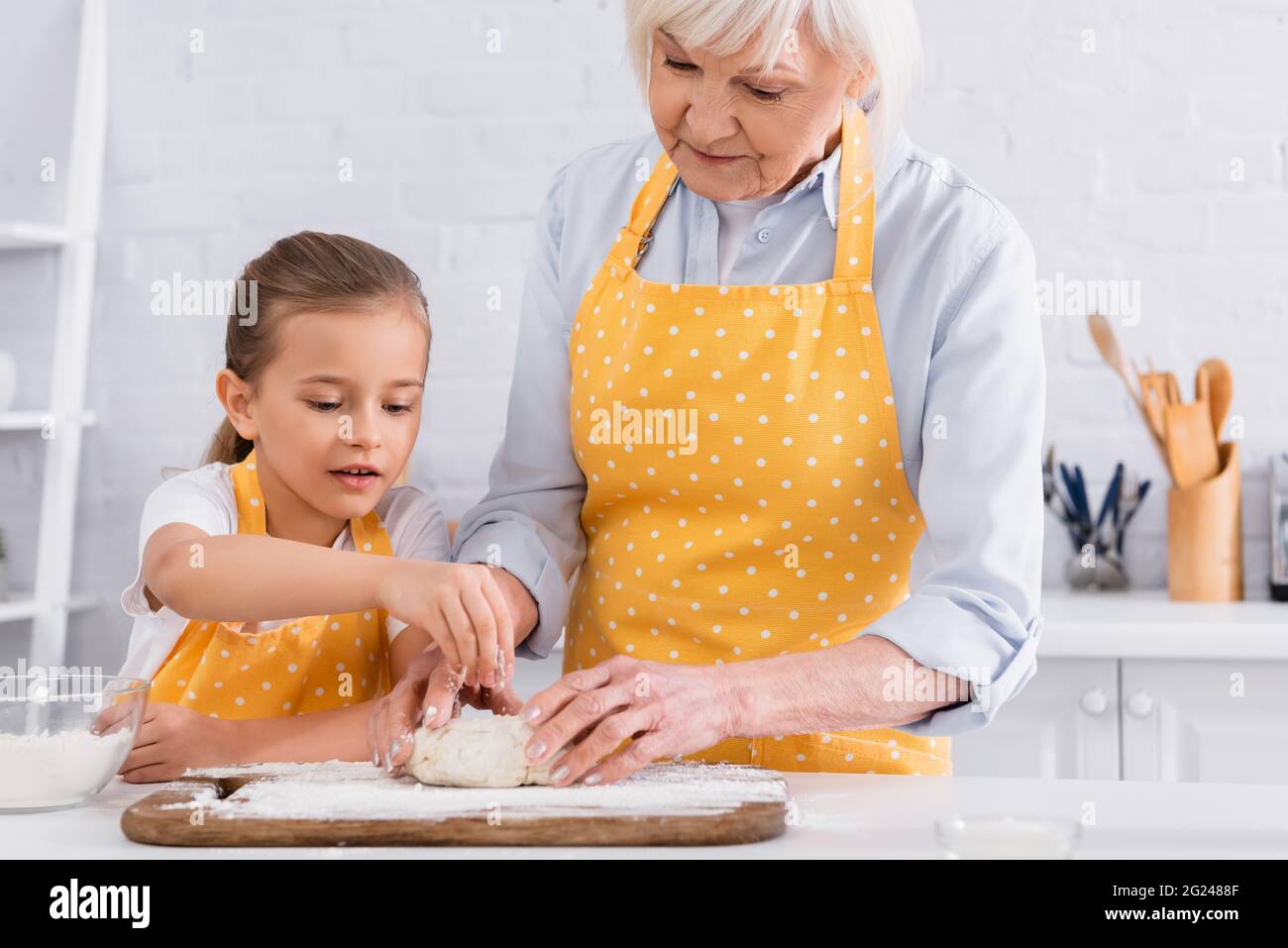 Kid and granny in aprons making dough together in kitchen Stock Photo ...