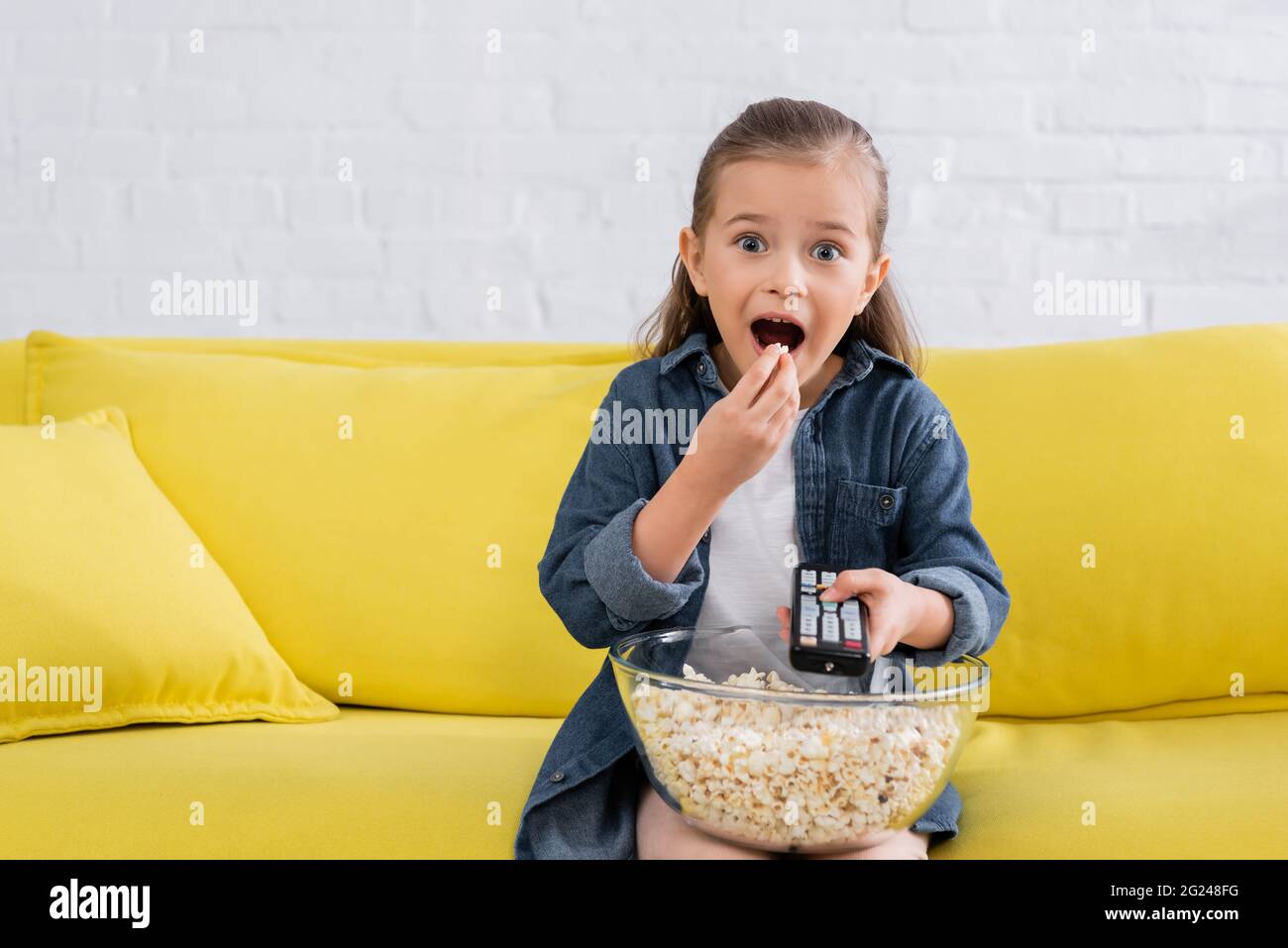 Excited girl with remote controller eating popcorn Stock Photo - Alamy