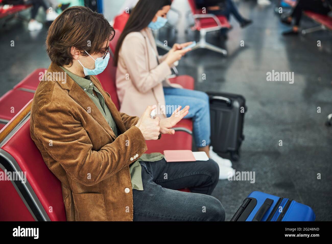 Stylish man in medical mask using hand sanitizer at airport Stock Photo ...
