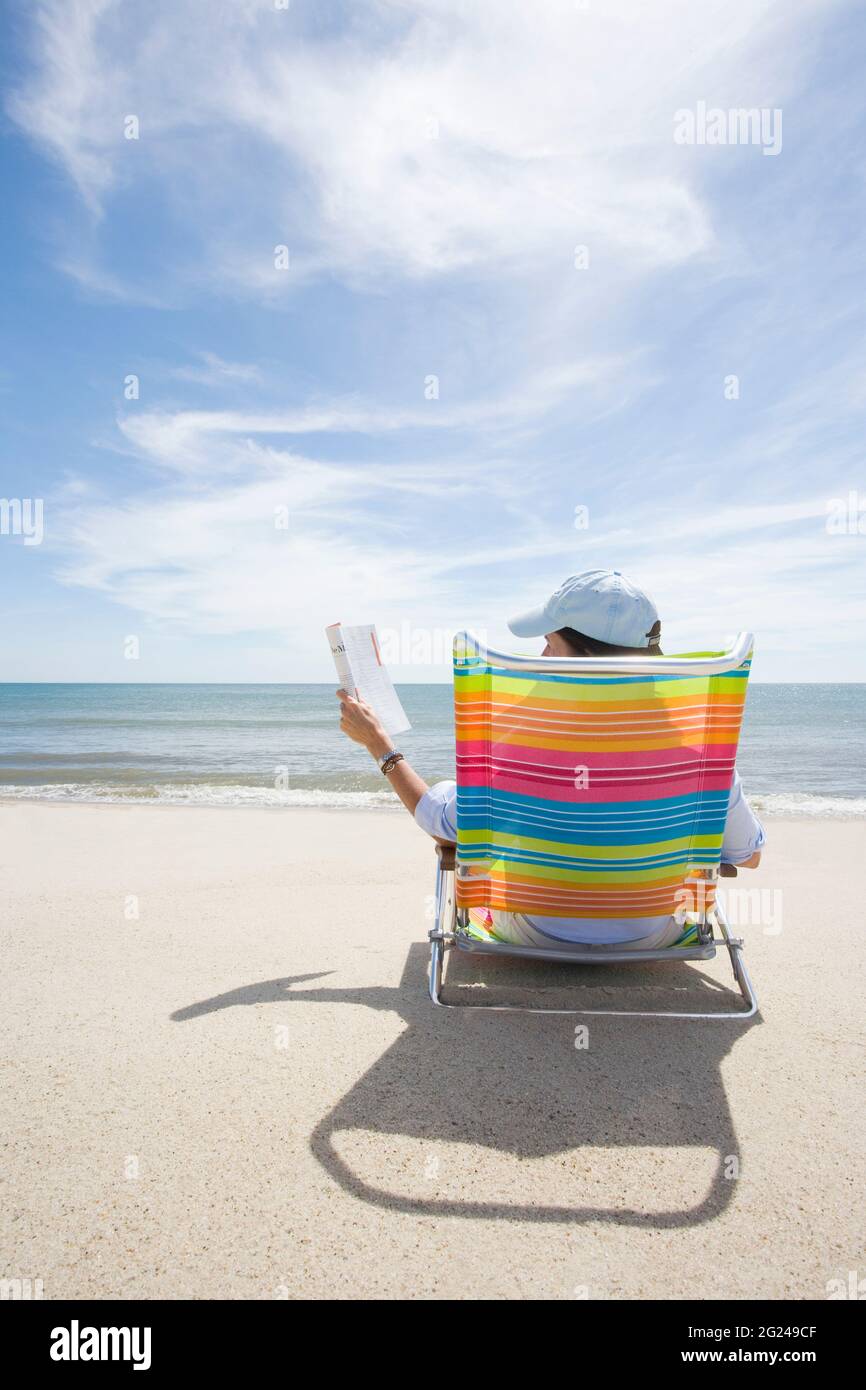 USA, Massachusetts, Cape Cod, Nantucket Island, Rear view of woman on colorful beach chair reading magazine on beach Stock Photo