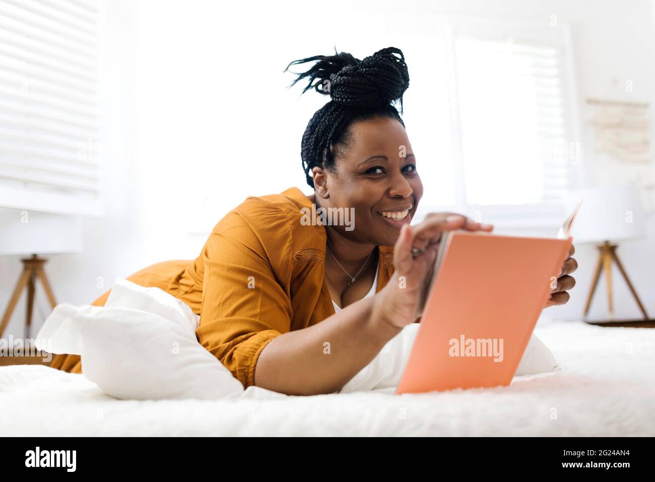 Smiling woman reading book in bed Stock Photo