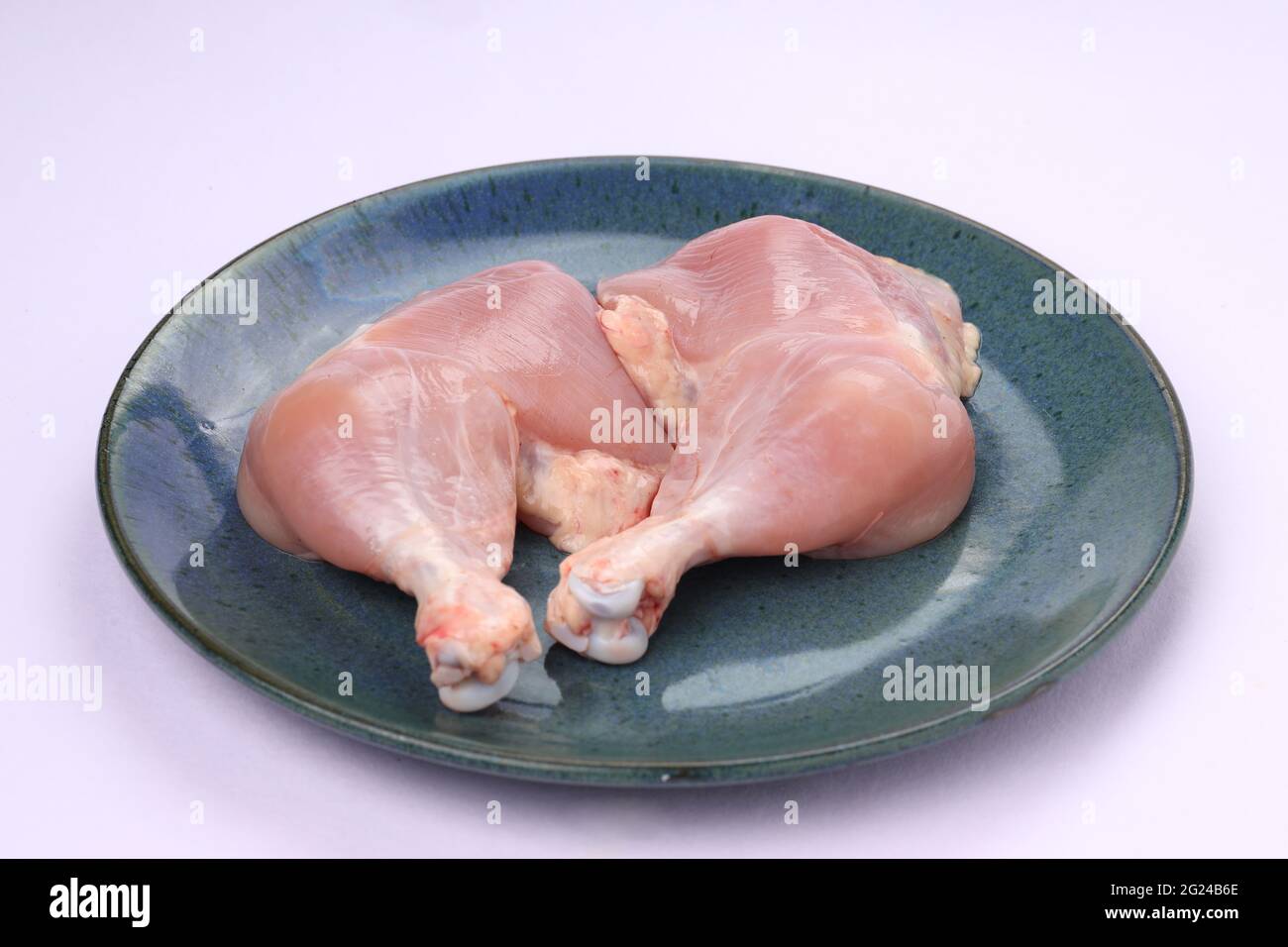 Raw whole chicken leg without skin arranged in a aqua rustic blue plate