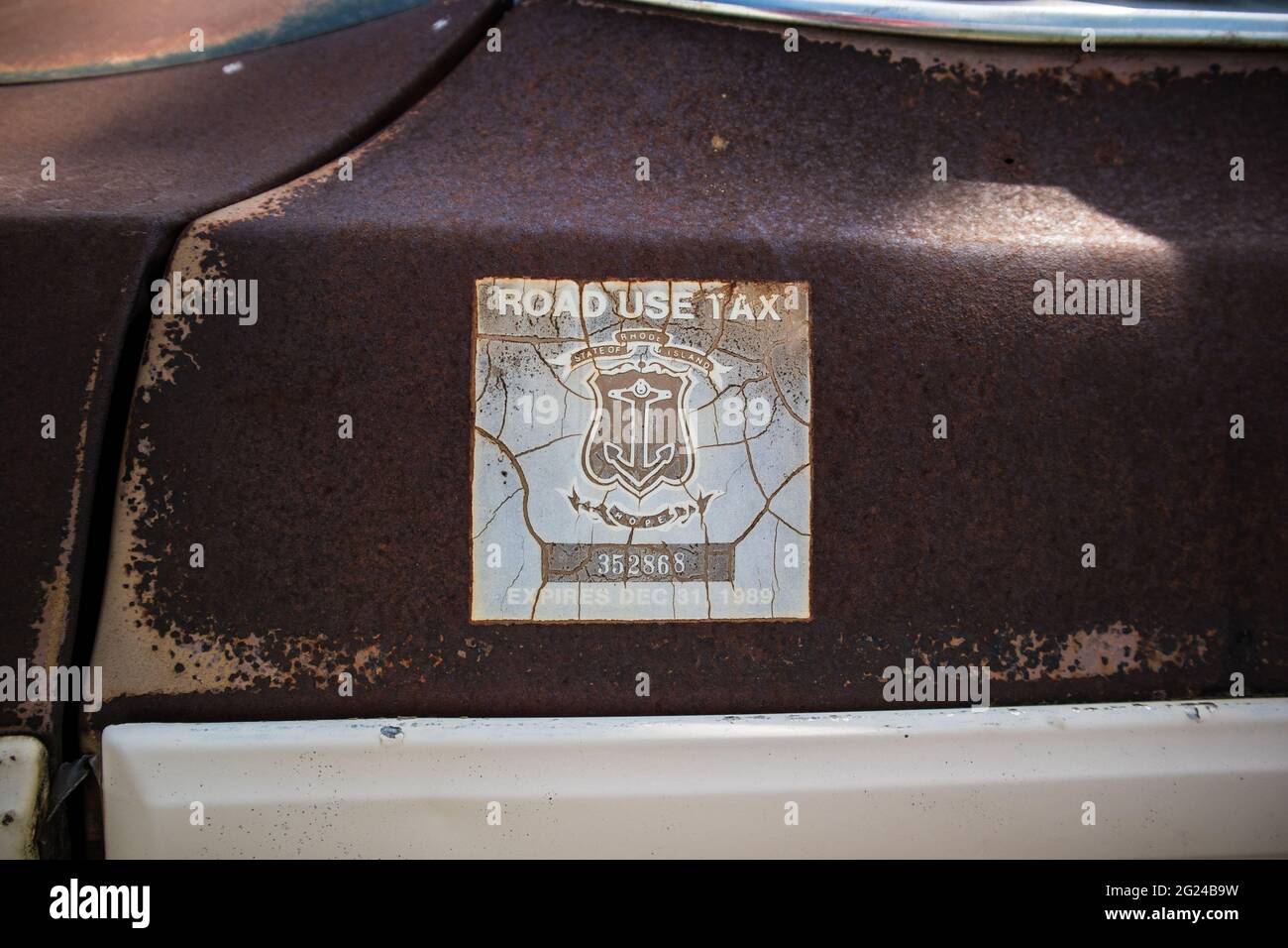 Rhode Island State: A Road Use Tax sticker that expired in December 1989 on the rust door of a wreck car Stock Photo