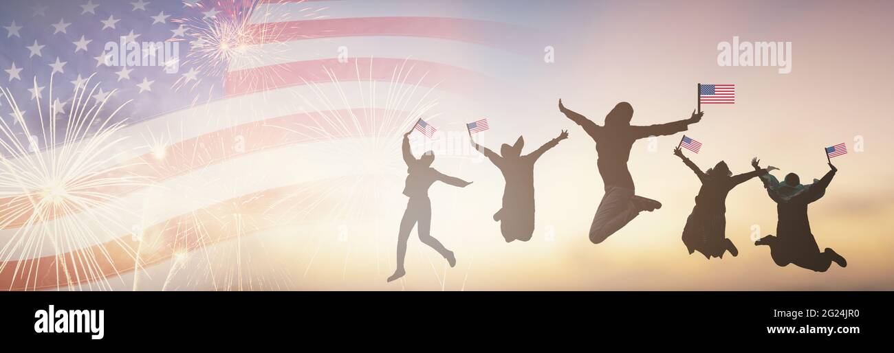 Silhouettes group of people holding the Flag of the USA jump in America celebrate 4th of July fireworks.  Waving happy American Flags at Sunset. Crowd Stock Photo