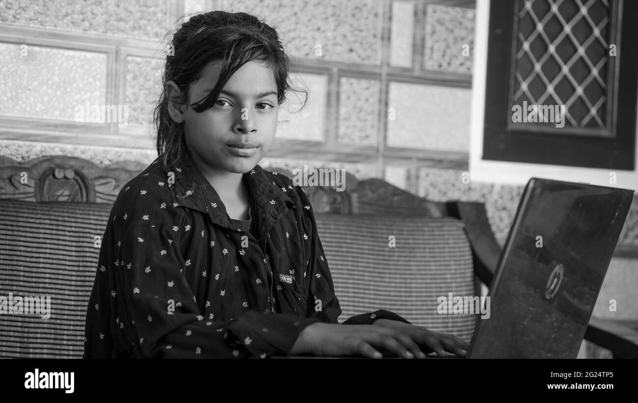 Cute Indian young girl looking at camera , Computer working at home sitting at table. Work from home concept. Stock Photo