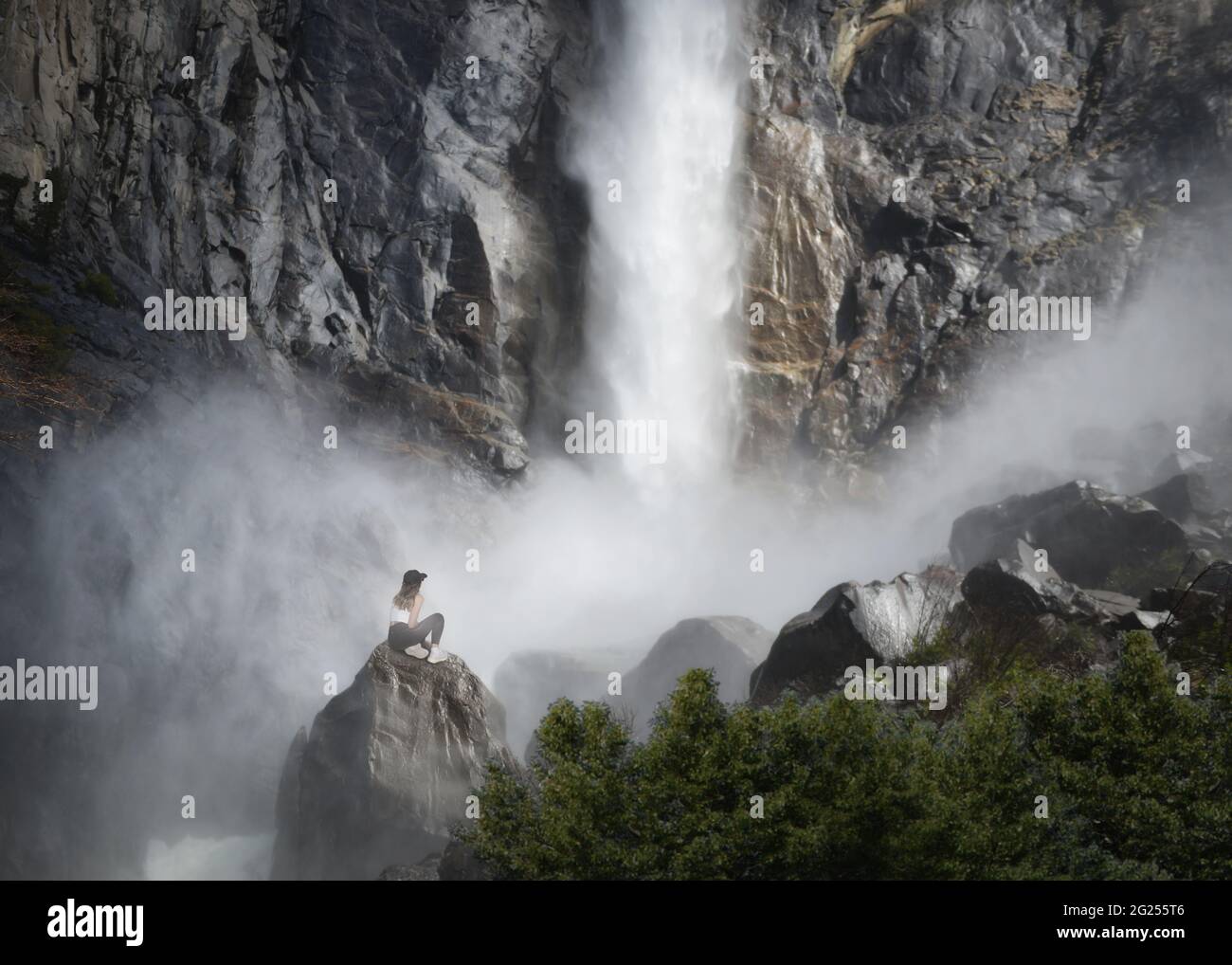 Woman sitting on a rock at the base of Bridalveil Fall, Yosemite National Park, California, USA Stock Photo