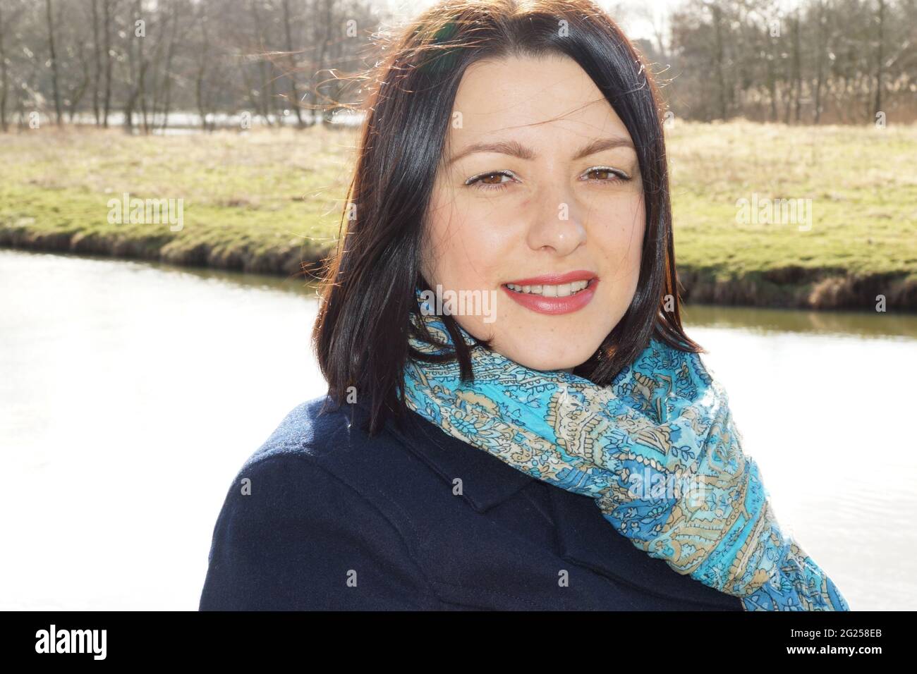 Smiling  Netherlandian brunette with a blue scarf posing with a river and field on background Stock Photo