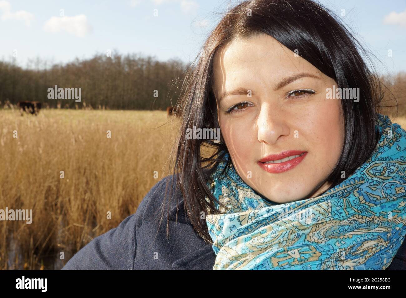 Smiling Netherlandian brunette with a blue scarf posing with a field on the background Stock Photo