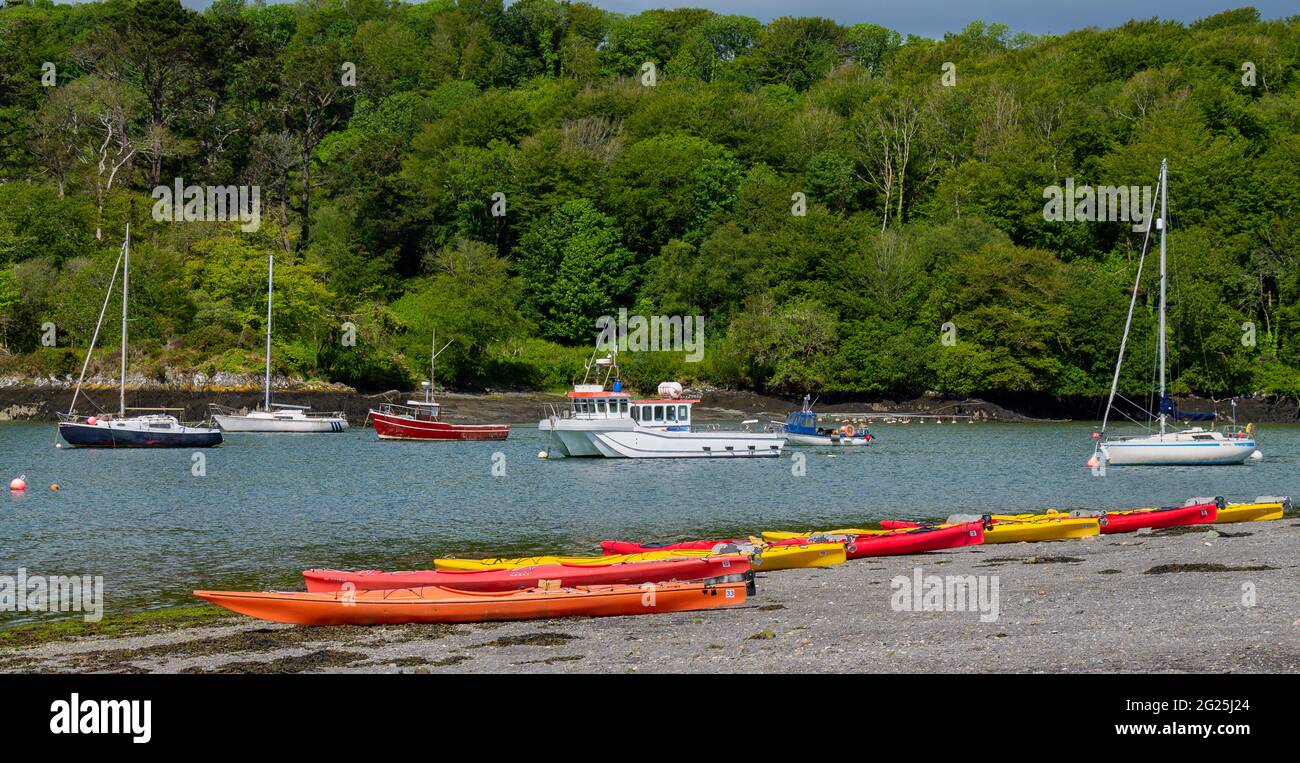 Kayaks pulled up on pebble beach with yachts anchored in tidal estuary Stock Photo
