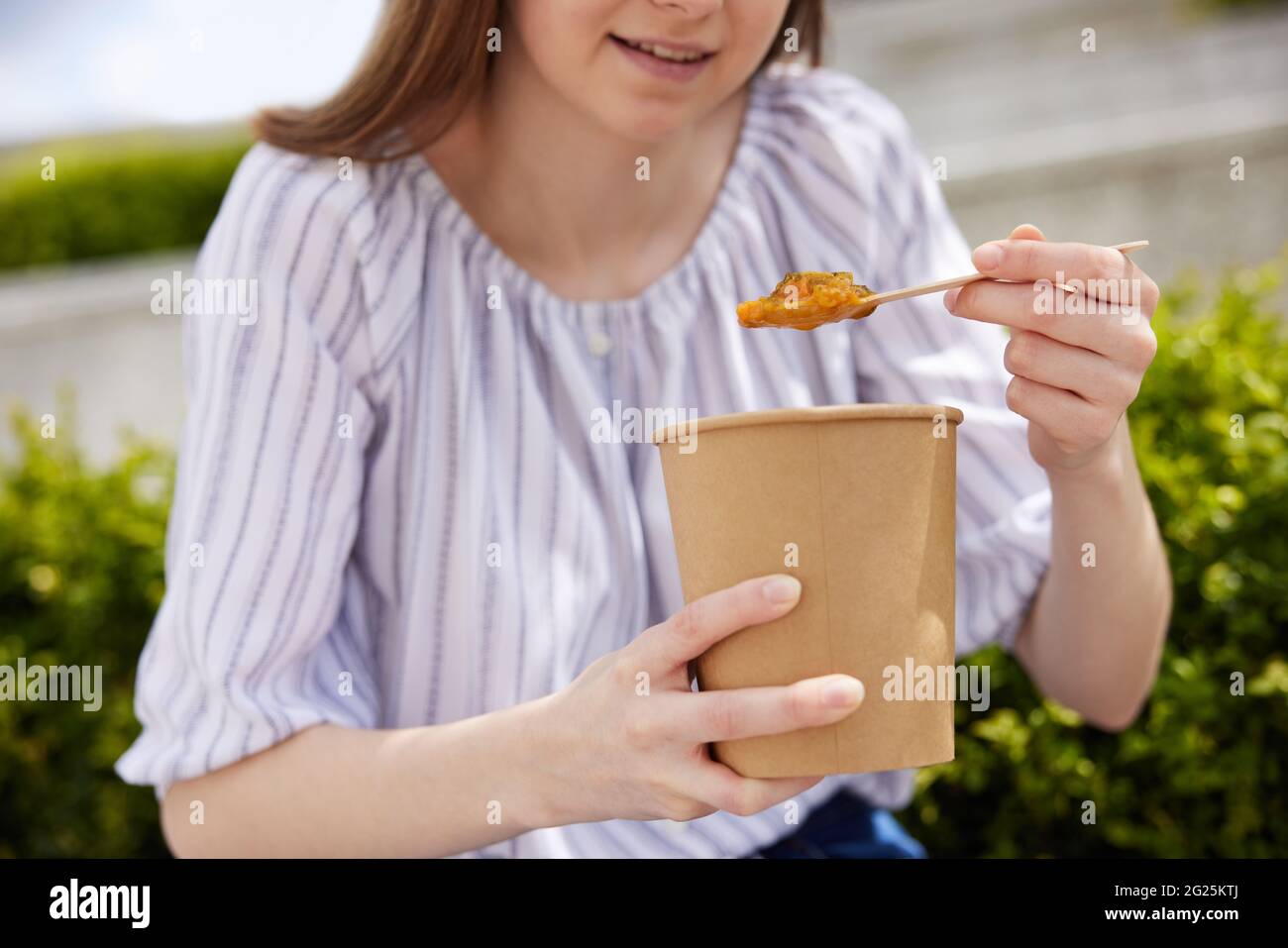 Close Up Of Woman Eating Healthy Vegan Or Vegetarian Soup As Takeaway Lunch From Recyclable Packaging With Wooden Spoon Stock Photo