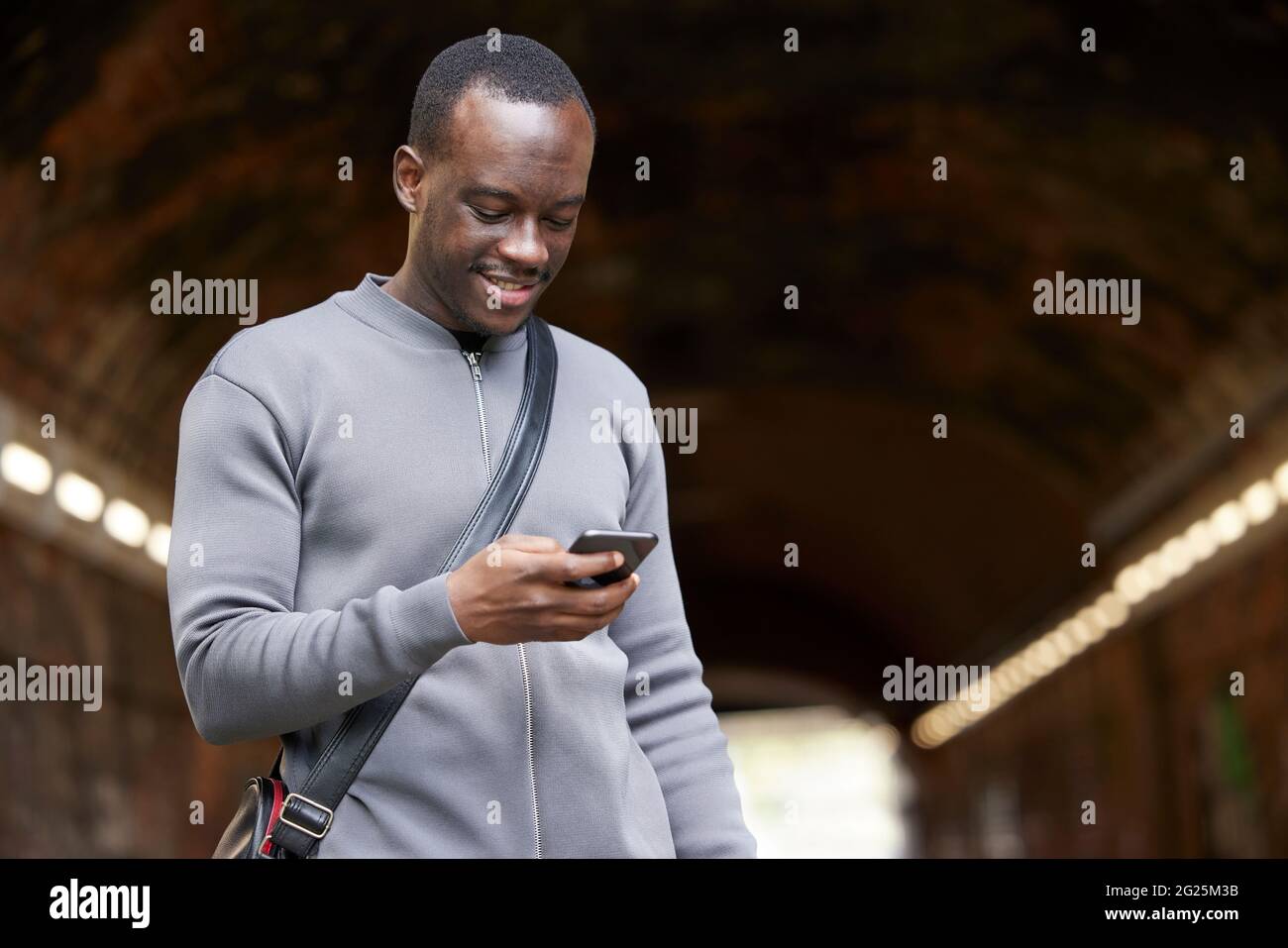 Smiling Young Man In Urban Setting Checks Messages And Social Media On Mobile Phone Stock Photo