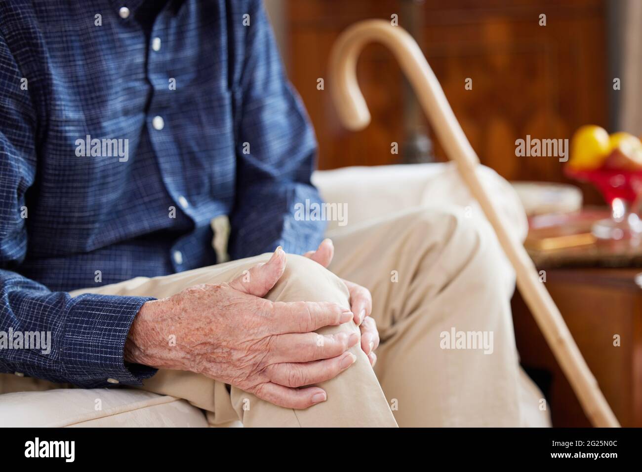 Close Up Of Senior Man Sitting On Sofa At Home Suffering With Knee Pain From Arthritis Stock Photo